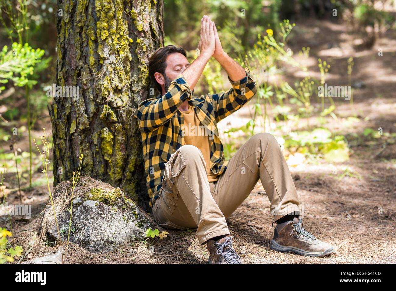 Erwachsener Mann im Wald sitzt auf dem Boden und meditiert und verliebt sich in den Wald draußen in der Natur - Konzept eines gesunden Lebensstils und glücklicher, friedlicher Menschen Stockfoto