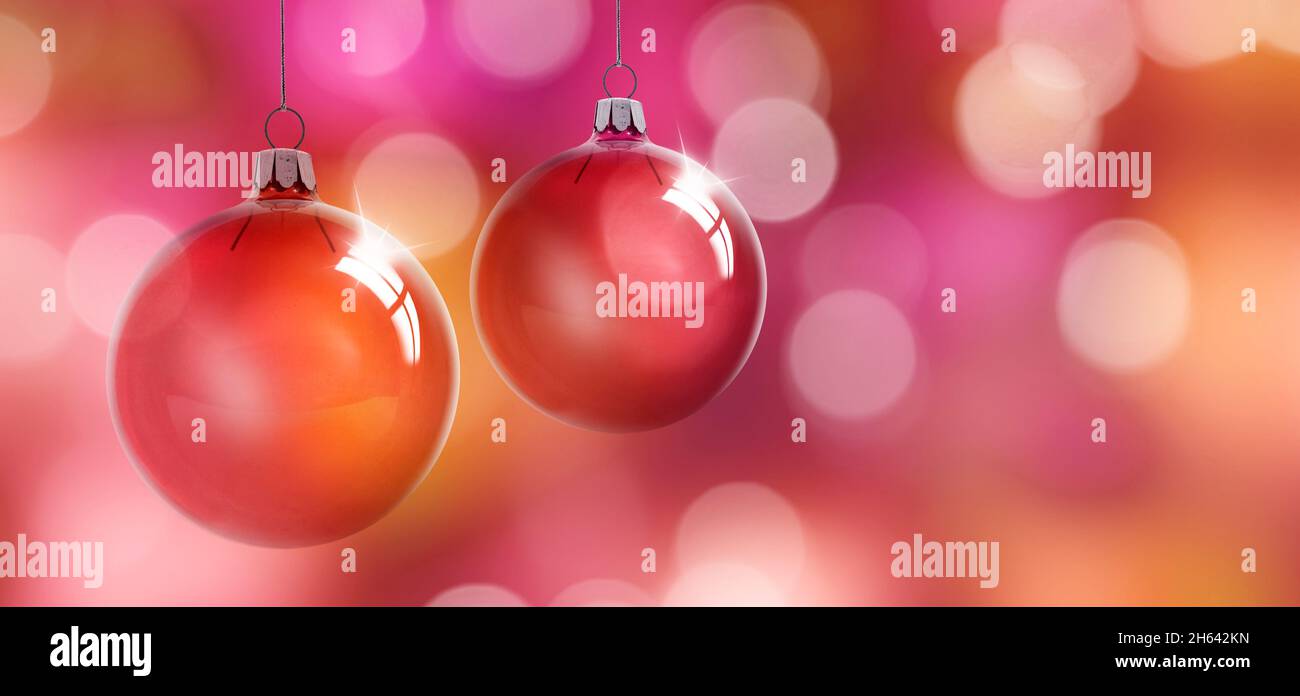 Zwei rote weihnachtskugeln vor einem unscharfen, farbenfrohen Hintergrund mit Lichtreflexionen Stockfoto