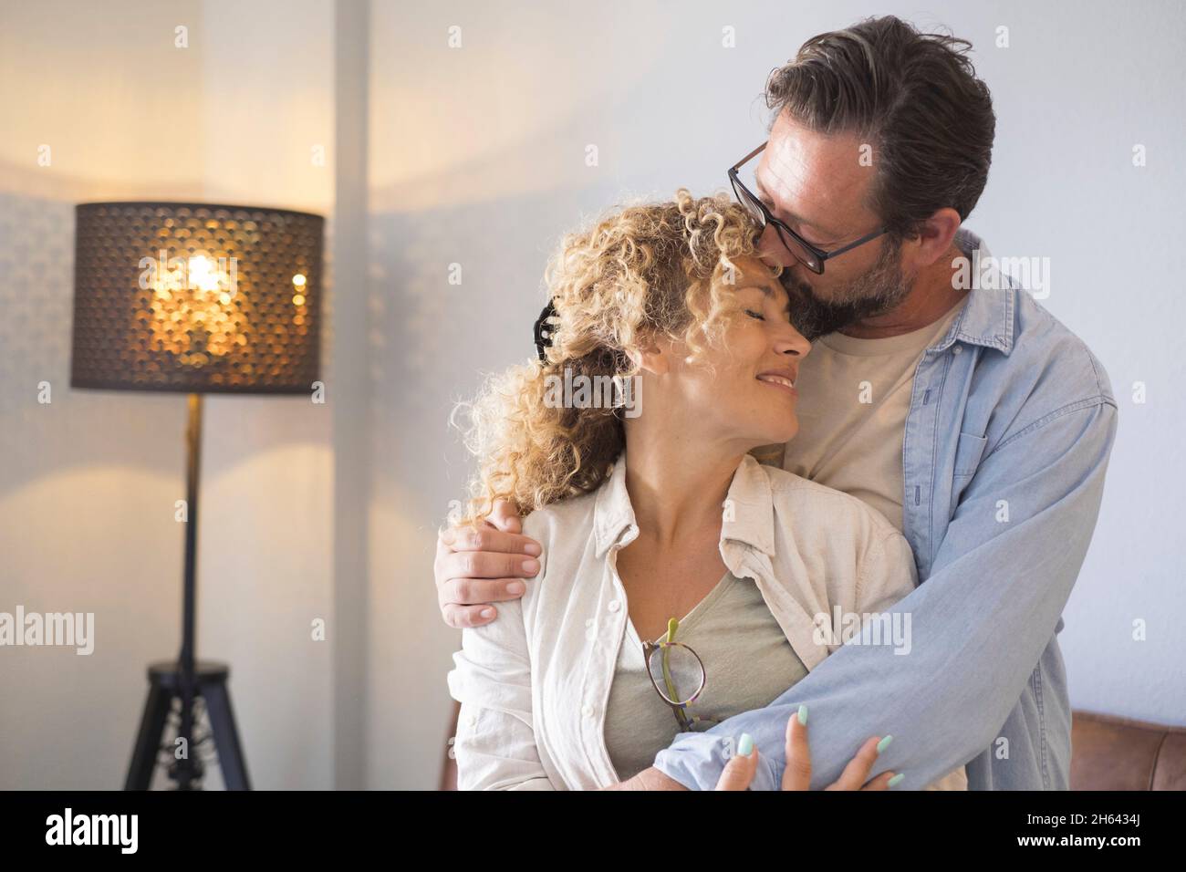 Paar umarmen und romancing stehen im Wohnzimmer zu Hause. Mann küsst Stirn der Frau mit Zuneigung. Liebevolles Paar Freizeit zusammen zu Hause verbringen Stockfoto