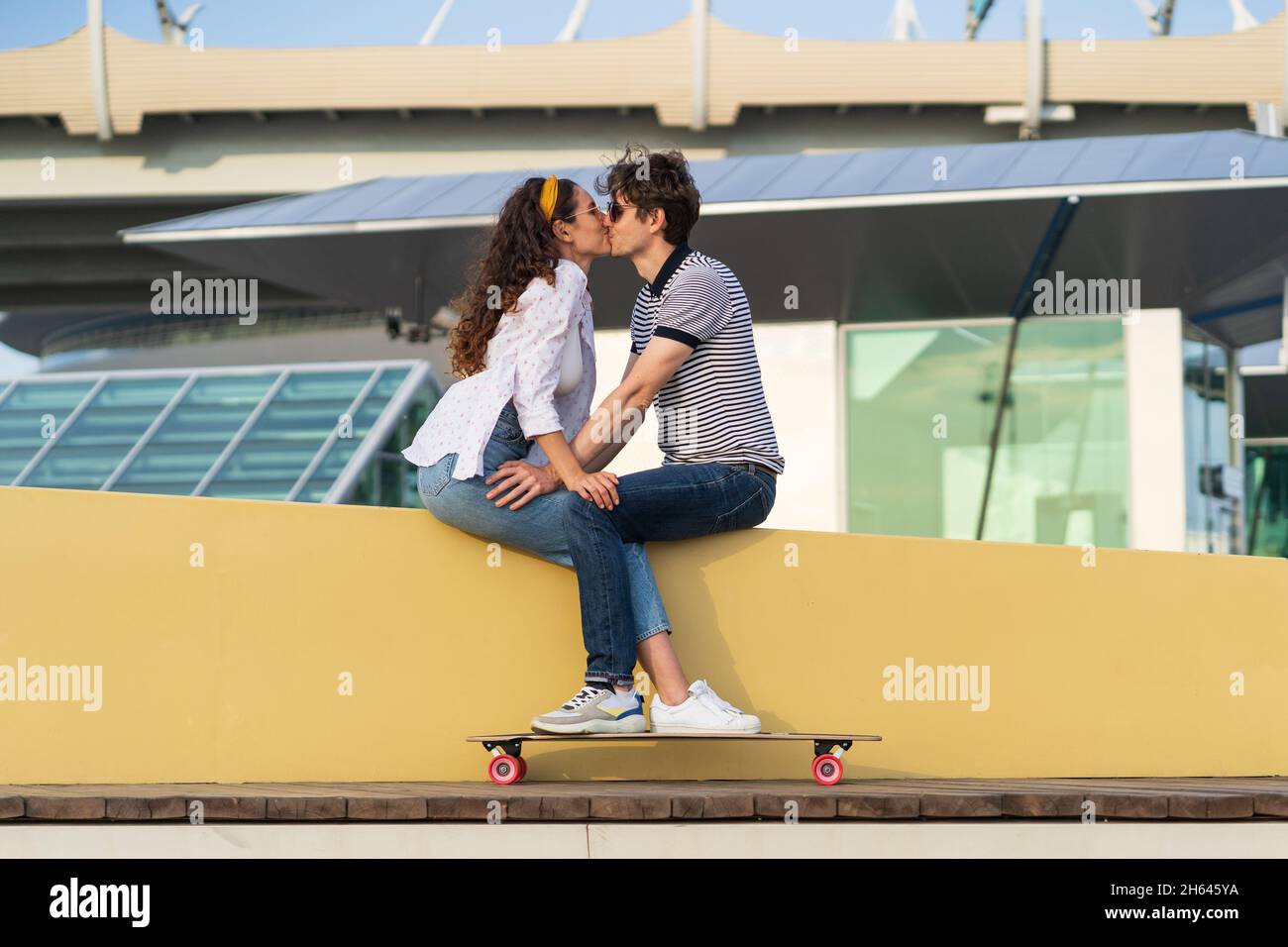 Stilvolles Paar küsst sitzen im Skatepark. Junge nette Longboarder Mann und Frau in Liebe kuscheln Stockfoto