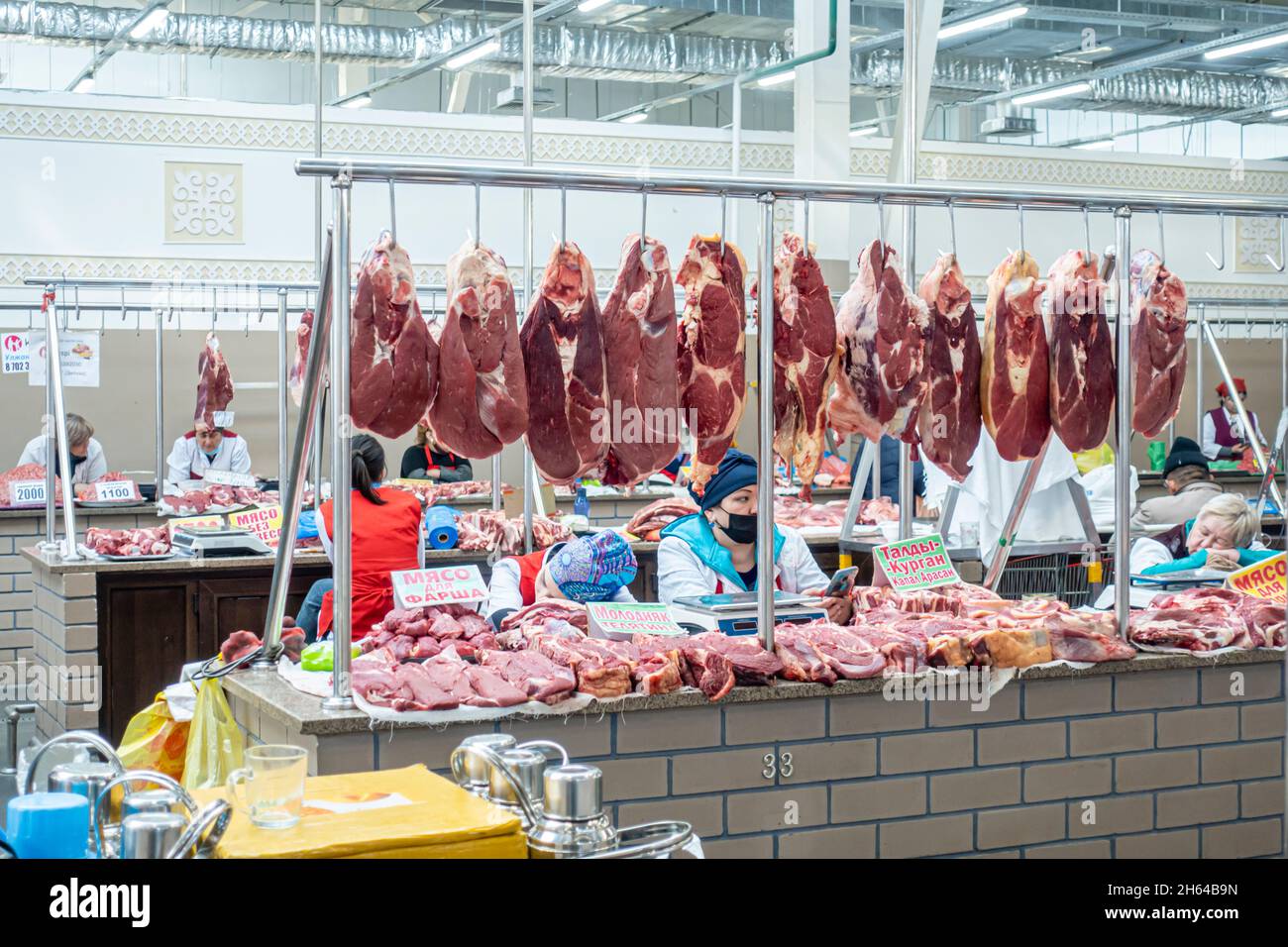 Rohes Fleisch zeigt den Altyn Orda Markt, den größten Markt in Almaty, Kasachstan. Schneiden Sie Fleischstücke hängen; Händler hinter Theken. Stockfoto