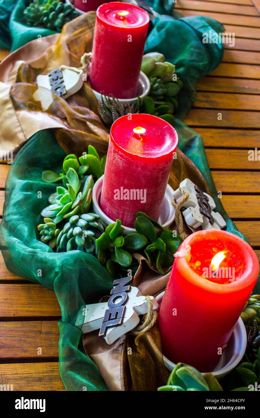 Ein Sommerweihnachtszentrum, bestehend aus drei brennenden Kerzen, umgeben von Sukkulenten, Holzdekorationen und glänzenden Bronze- und grünen Stoffen. Stockfoto