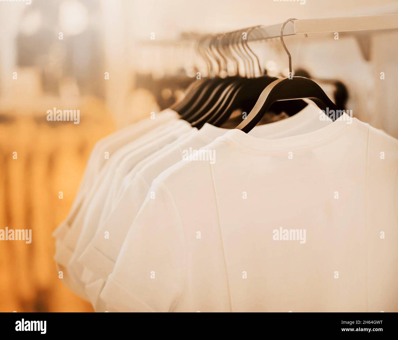 Einfache, legere weiße T-Shirts hängen in einem Bekleidungsgeschäft an schwarzen Kleiderbügeln, die von Licht beleuchtet werden. Einkaufen und Verkauf. Bequeme Kleidung. Stockfoto