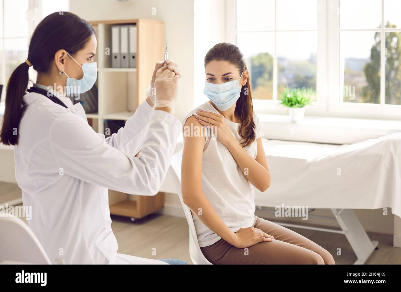 Krankenschwester, die eine Spritze vorbereitet, um eine weibliche Patientin im Impfzentrum mit einer Injektion zu impfen. Stockfoto