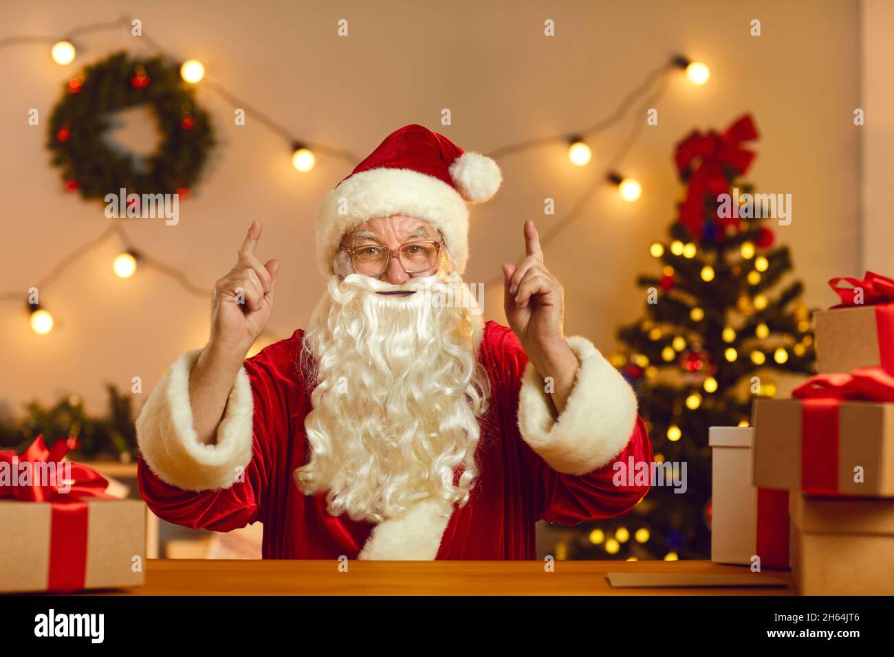 Santa sitzt am Schreibtisch in der Werkstatt, schaut während eines Videoanrufs auf die Kamera und teilt interessante Ideen Stockfoto