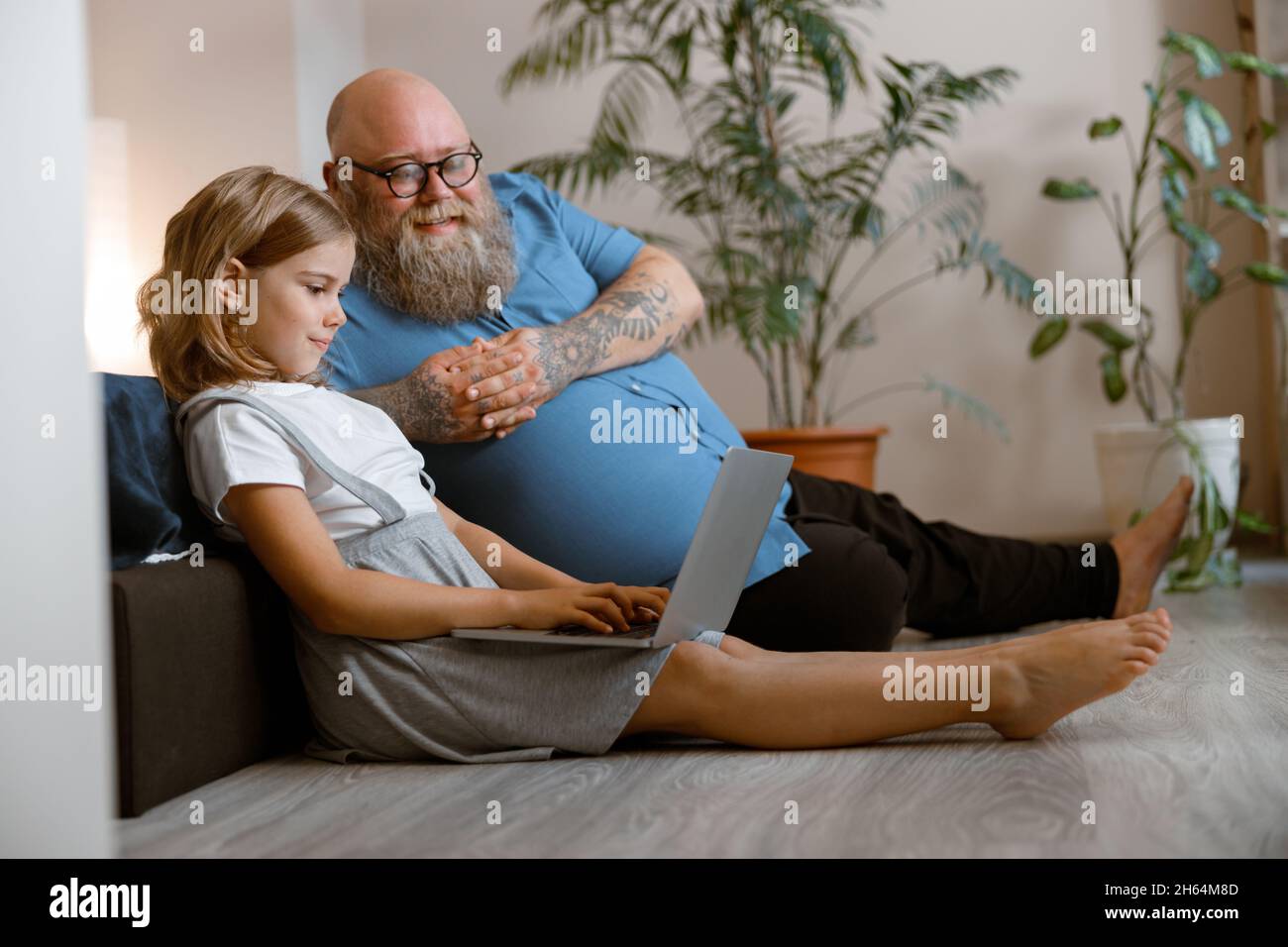 Lächelnder Vater und niedliches Mädchen sehen sich Videos über einen Laptop an, der auf dem Boden im Schlafzimmer sitzt Stockfoto