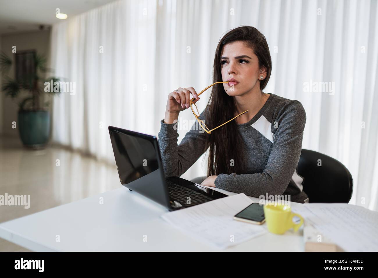 Nachdenkliche Lateinerin, die mit einem Laptop auf dem Tisch sitzt, denkt an Inspiration, träumt davon, tief in Gedanken verloren zu blicken, verträumte Schriftstellerin mit Compu Stockfoto