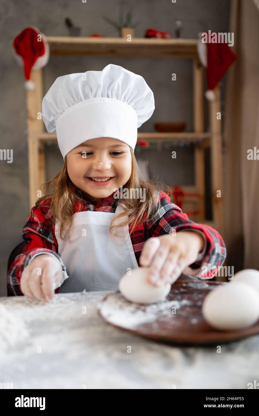 Kleines Bäckermädchen. Das Kind bereitet Weihnachts-Lebkuchen oder Keks und nimmt Eier vom Teller. Portrait von Kinderkoch mit hausgemachten gebacken Stockfoto