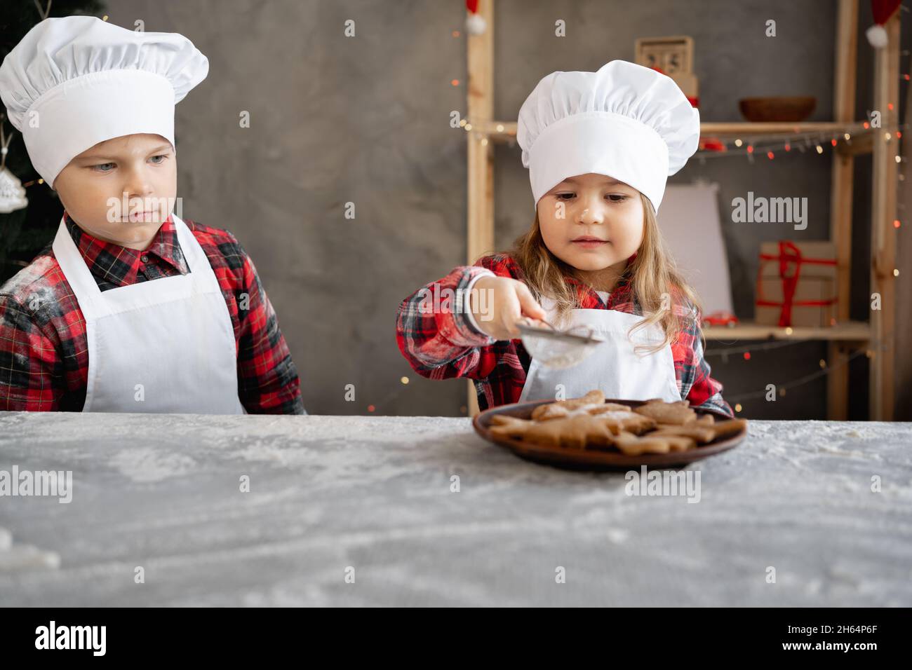 Kinder kochen WeihnachtsLebkuchen. Bruder und Schwester dekorieren in der Küche Kekse mit Puderzucker. Kleines Bäckermädchen. Hausgemachte Kuchen. Stockfoto