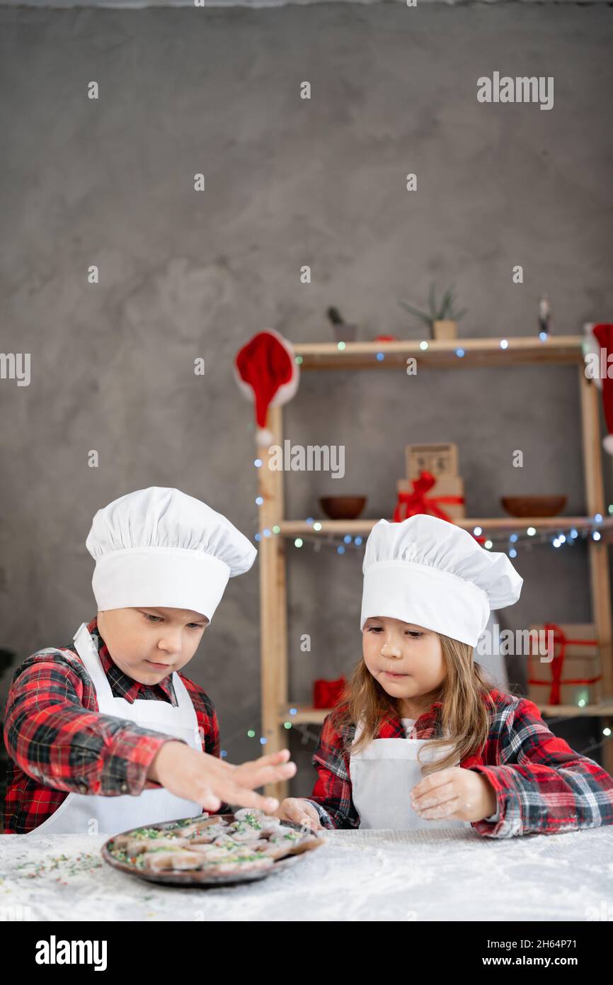 Bruder und Schwester schmücken Lebkuchen und Kekse zu Weihnachten. Kinder kochen zu Hause für den Urlaub. Vertikale Ansicht. Stockfoto