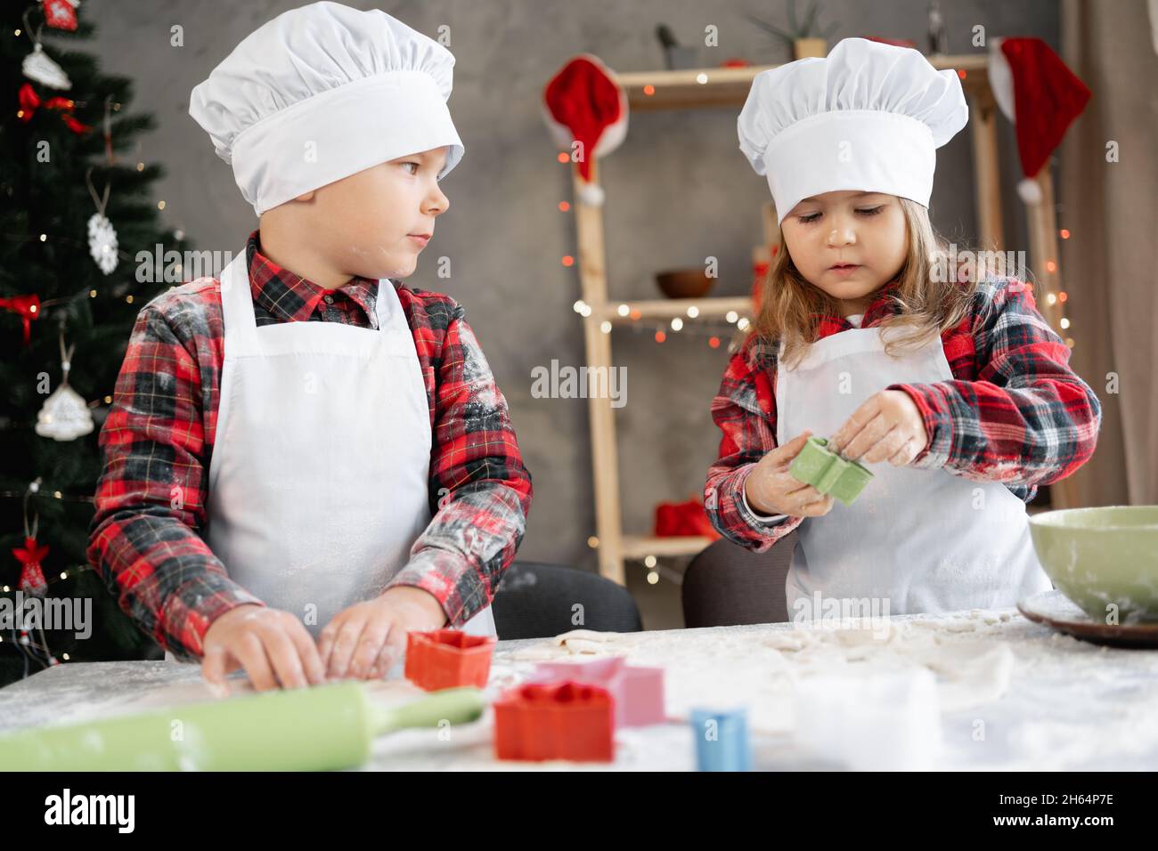 Der kleine Bruder und die Schwester bereiten in der Küche Weihnachtsplätzchen zu, die Kinder schneiden Teig mit einer Form aus und backen in der Küche. Festlich Stockfoto