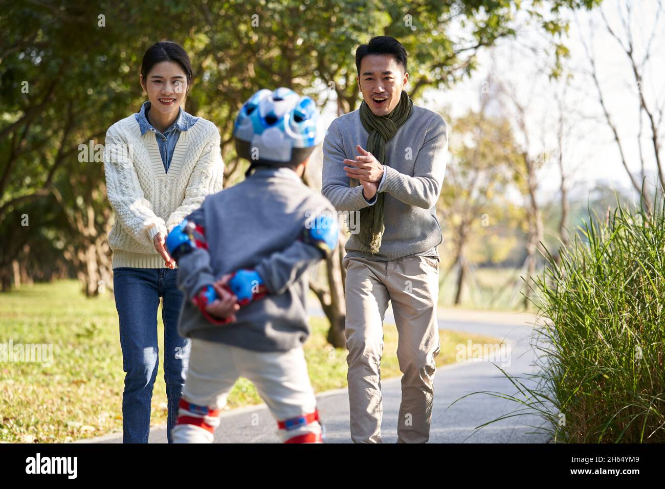 Liebevolle asiatische Eltern lehren Sohn Rollschuh im Freien im Stadtpark Stockfoto