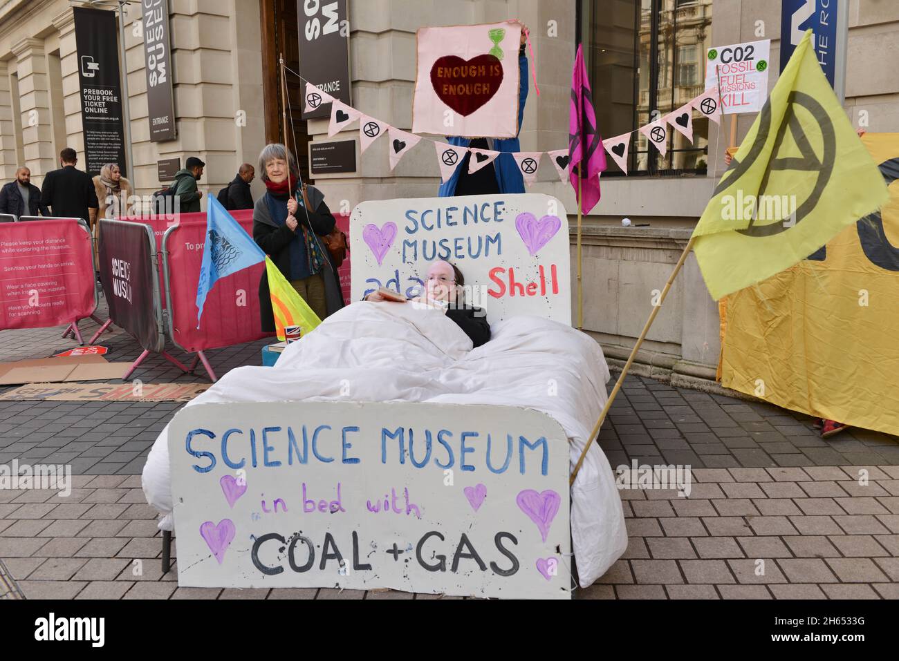 Ein als Direktor des Science Museums gekleideter Protestler Ian Blatchford liegt während der Demonstration auf einem Bett. Extinction Rebellion-Aktivisten veranstalteten einen Protest gegenüber dem Science Museum in South Kensington gegen das Sponsoring des Museums durch die fossilen Energiekonzerne Shell und Adani. Stockfoto