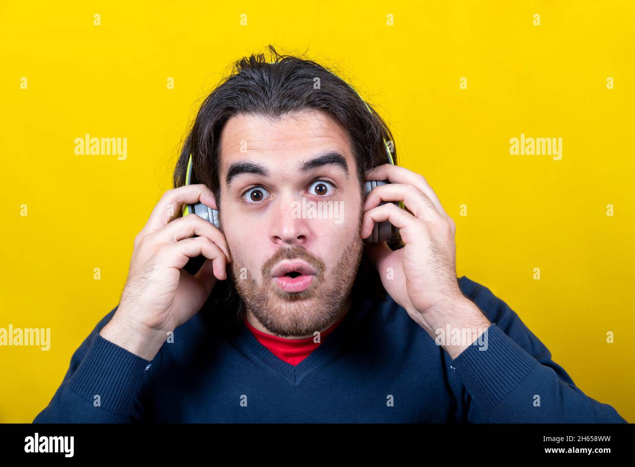 Der junge Mann, der in die Kamera schaut, ist überrascht über die Musik, die er mit Kopfhörern hört. Der Mann hat lange Haare, einen Bart und einen sehr tiefen Blick. C Stockfoto