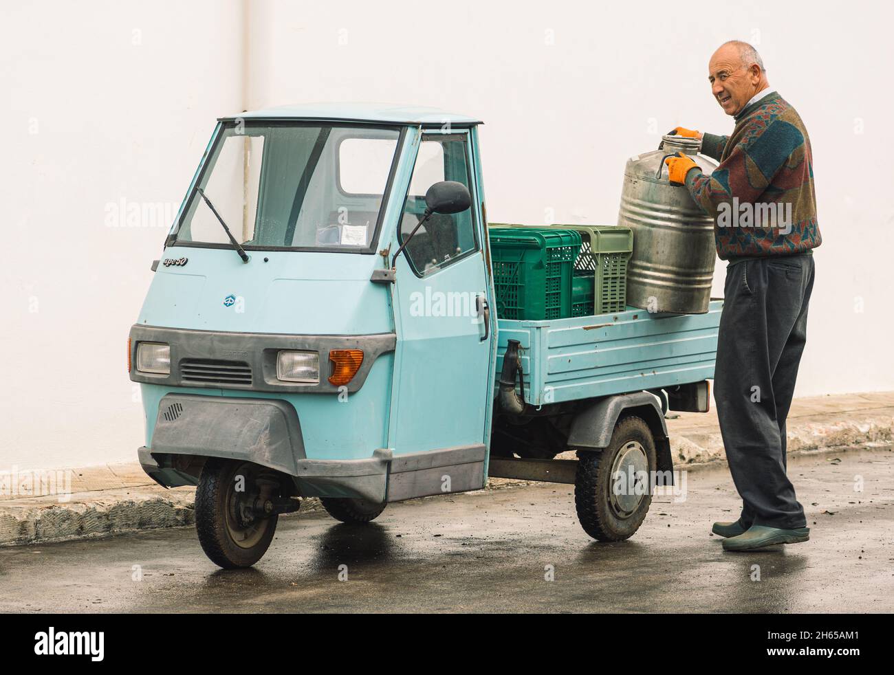 Ein alter Bauer mit einem alten, leichten kommerziellen Affe-Auto, das ein Olivenöl-Fass trägt, das gerade in Apulien, Italien, hergestellt wurde Stockfoto