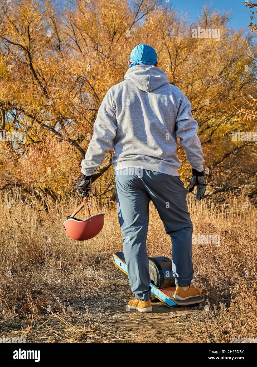 Senior Mann mit einem Rädern Elektro-Skateboard und Helm auf einem Feldweg in der Herbstlandschaft in Colorado Stockfoto