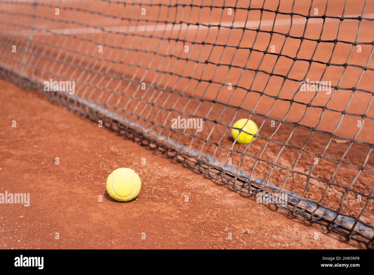 Zwei Tennisbälle, die durch ein Netz auf einem Sandplatz getrennt sind. Trainingskonzept für Sportturniere Stockfoto