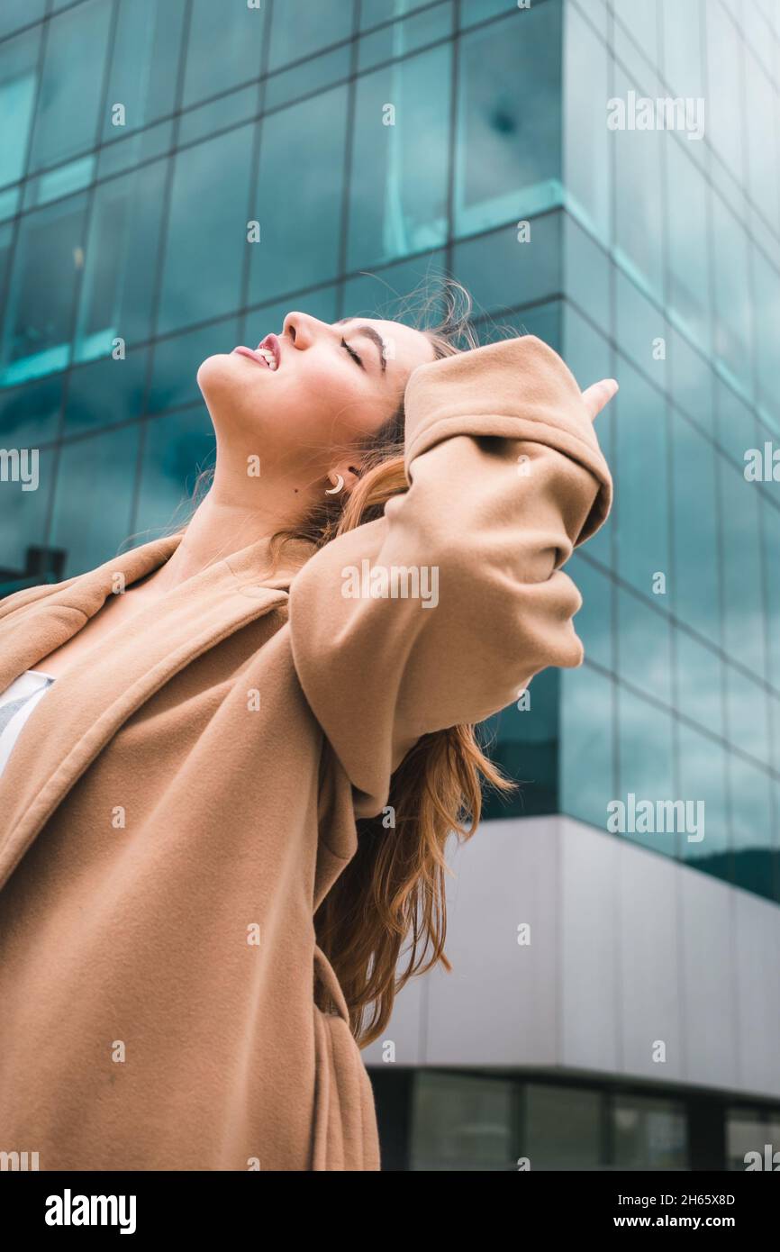 Starke hispanische Frau vor blauen Gebäudefenstern, die Selbstvertrauen ausstrahlen Stockfoto