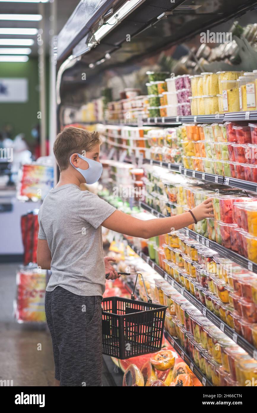 Chicago, IL, 21. August 2021: Kind mit Maske, Einkaufen im Supermarkt. Kommissionierung frisch geschnittener Früchte und Gemüse – Pandemiekonzept, für redaktionelle U Stockfoto