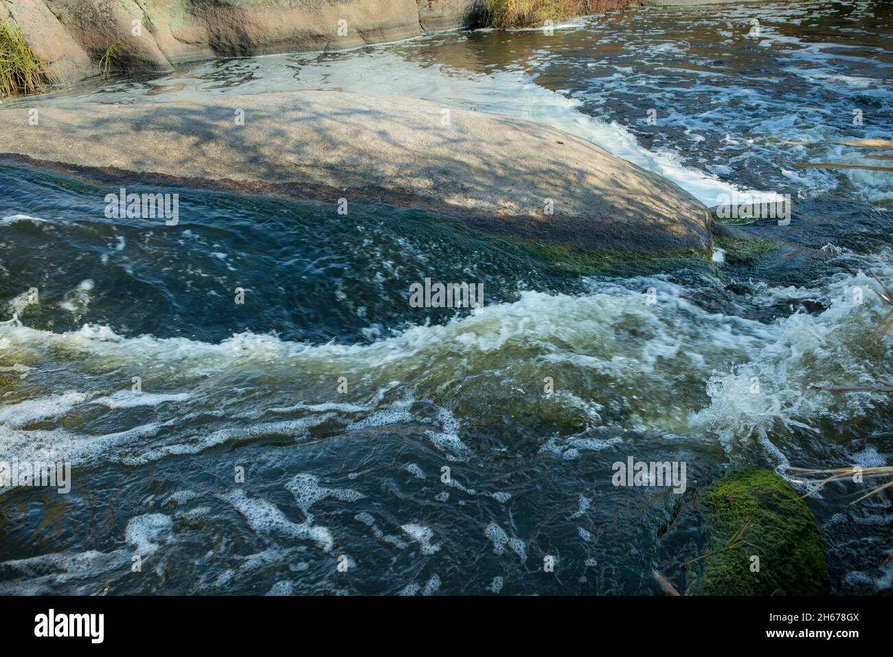 Abstrakter Hintergrund. Die Wellen des Süßwassers treffen sich mit den spitzen Unterwasserfelsen, die Whirlpools bilden. Whirlpools in der Region des einzigen Steppenwaterfals Stockfoto