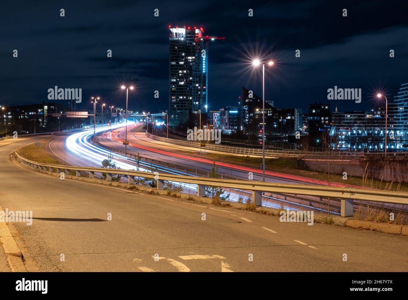 Helsinki / Finnland - 13. NOVEMBER 2021: Umgehungsfahrzeuge, die leichte Wege auf der Autobahn werfen, während der moderne Stadtteil im Hintergrund liegt Stockfoto