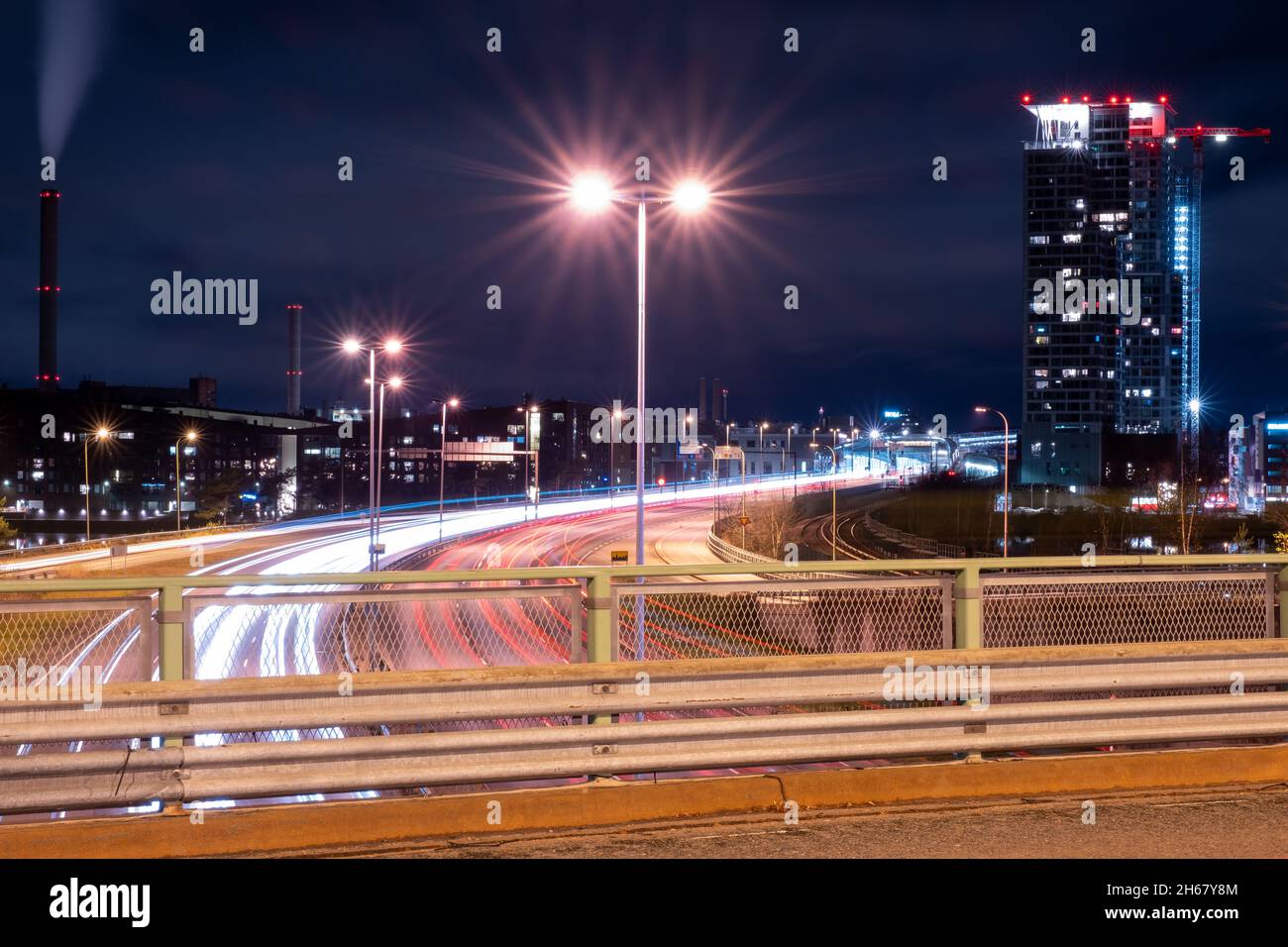 Helsinki / Finnland - 13. NOVEMBER 2021: Umgehungsfahrzeuge, die leichte Wege auf der Autobahn werfen, während der moderne Stadtteil im Hintergrund liegt Stockfoto