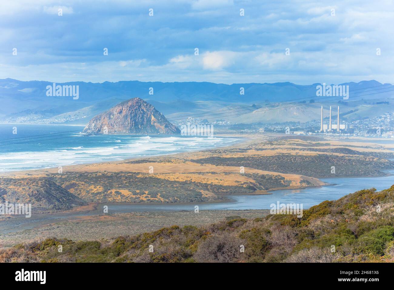 Morro Bay. Blick vom Montana de Oro State Park. Klippen, Sandstrand, Morro Rock, Berge und wolkiger Himmel im Hintergrund, California Central Coast Stockfoto