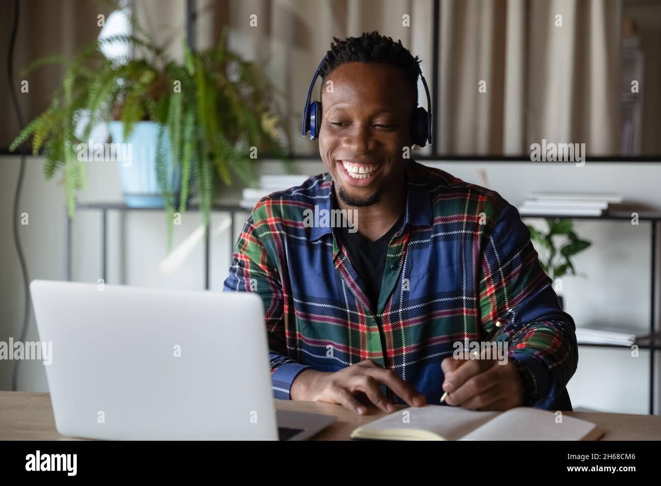 Fröhlicher junger afroamerikanischer Mann mit Kopfhörern, der pädagogische Vorträge hört. Stockfoto