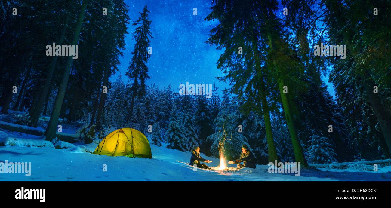 Pärchen campen mit Lagerfeuer und Zelt im Freien im Winterwald Stockfoto
