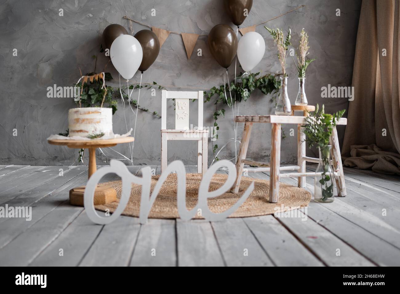 Fotozone zum ersten Geburtstag, Kuchen und Luftballons im rustikalen Stil, Holzboden, grauer Wandhintergrund. Stockfoto