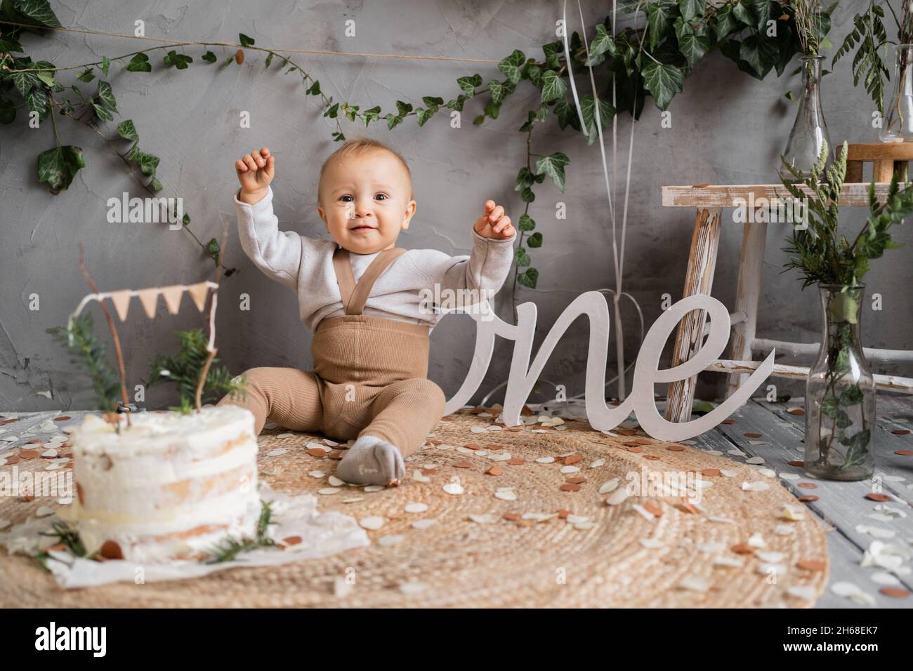 Alles gute zum Geburtstag, ein Jahr Kleinkind, Junge mit Kuchen auf dem Boden sitzend, natürlicher Hintergrund, rustikales Dekor. Stockfoto