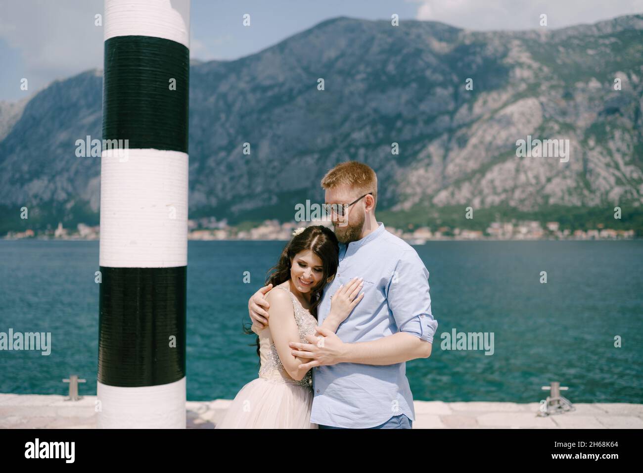Braut und Bräutigam umarmen sich am Pier in der Nähe des Leuchtturms in der Bucht von Kotor Stockfoto