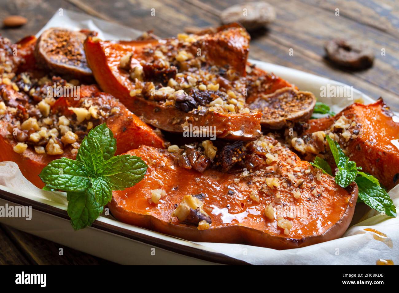 Gebackene Kürbisscheiben mit Nüssen, Honig und getrockneten Früchten auf einem hölzernen Hintergrund. Nahaufnahme. Richtige Ernährung, diätetische Mahlzeit. Nährwert von Gemüse Stockfoto