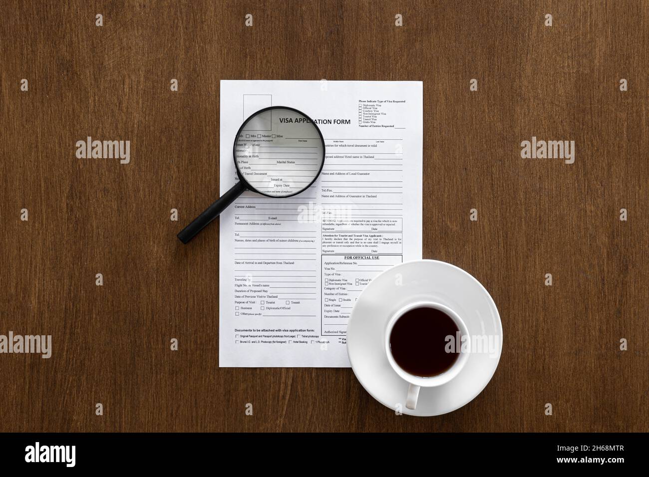 Visa-Antragsformular, Lupe und eine Tasse Kaffee auf einem Holzhintergrund. Stockfoto