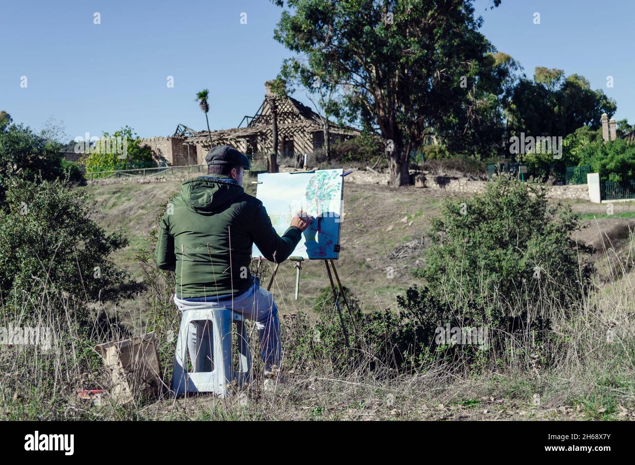 Mann malt eine Landschaft mit einem verlassenen Haus auf dem Land Stockfoto