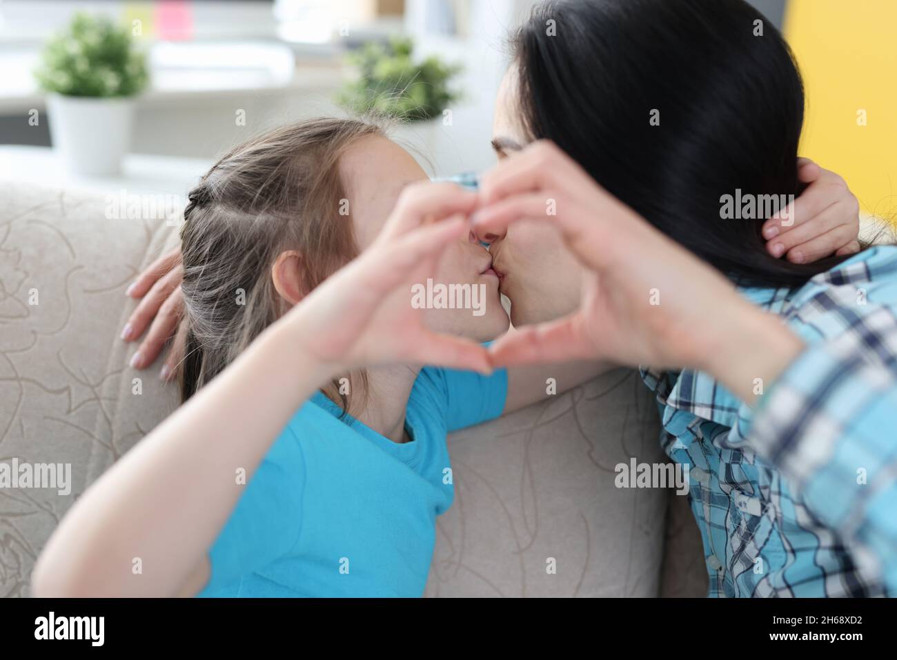 Mama küsst kleine Tochter, zusammen zeigen Herzensgesten Stockfoto