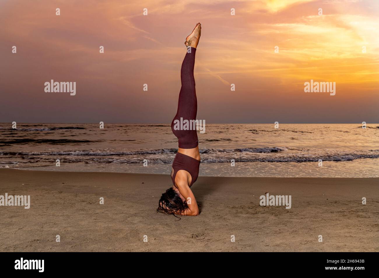 Frau praktiziert Yoga am Strand bei Sonnenuntergang. Frau in Sirsanlage auf dem Sand. Konzept von Wohlbefinden und Gelassenheit. Stockfoto