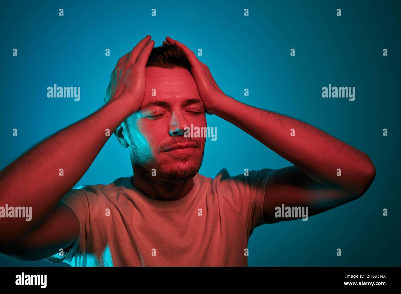 Porträt beleuchtet von Neonlicht. Erwachsene Männer in roten und grünen Lichtern haben den Kopf in den Händen. Stockfoto