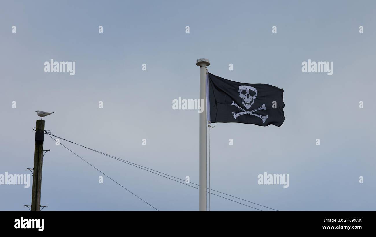 Schwarze Flagge mit Totenkopf und zwei sich kreuzenden Knochen, die im Freien fliegen. Stockfoto