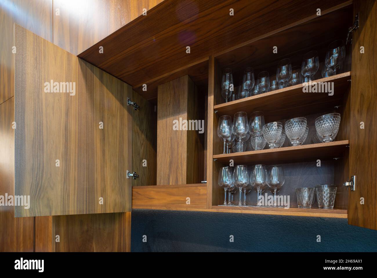 Modernes Interieur der Luxus-Wohnung. Stilvolle Holzküche. Schrank geöffnet. Gläser auf Regalen. Stockfoto