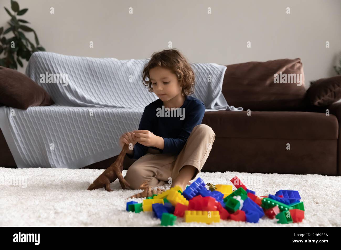 Kleiner Junge, der mit Spielzeug-Dinosaurier spielt und auf warmem Boden sitzt Stockfoto