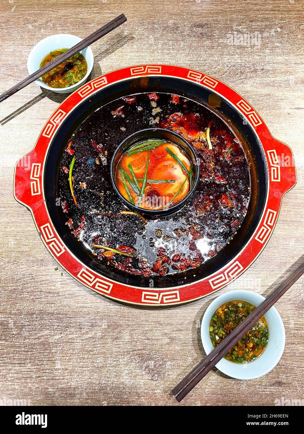 Würziger Sichuan-Hotpot mit Tomatensuppe, auf Holztisch des Hotpot-Restaurants, mit zwei Ölgerichten mit Essstäbchen Stockfoto