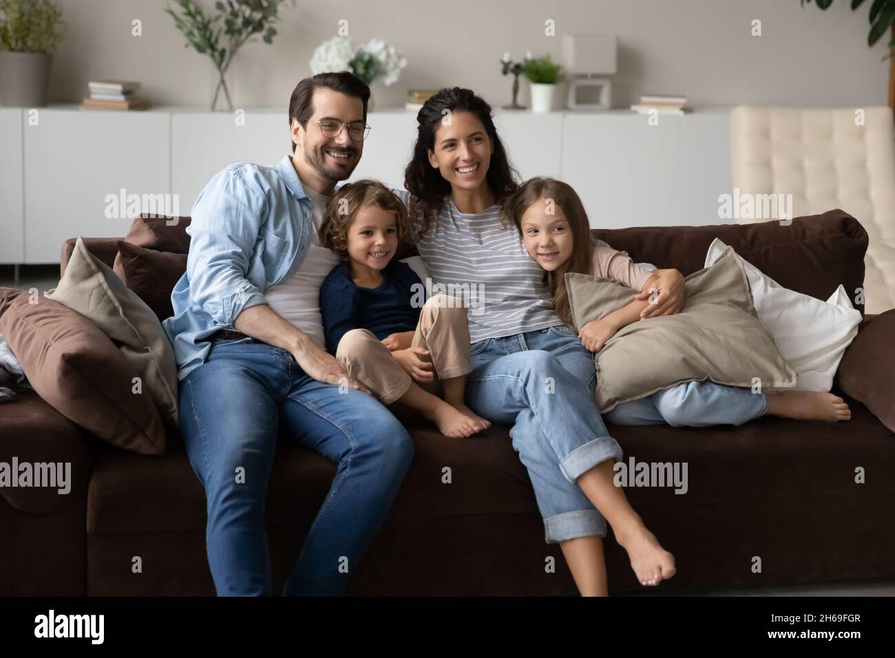 Glückliche Familie mit zwei kleinen Kindern, die auf einer bequemen Couch sitzen Stockfoto