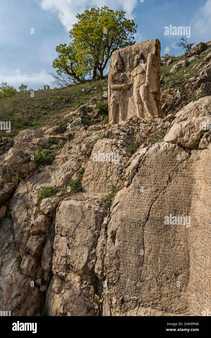 Steinskulpturen griechischer Gottheiten mit einer Steinmauer voller geschnitzter Schriften am Fuße des Berges der Götter Stockfoto