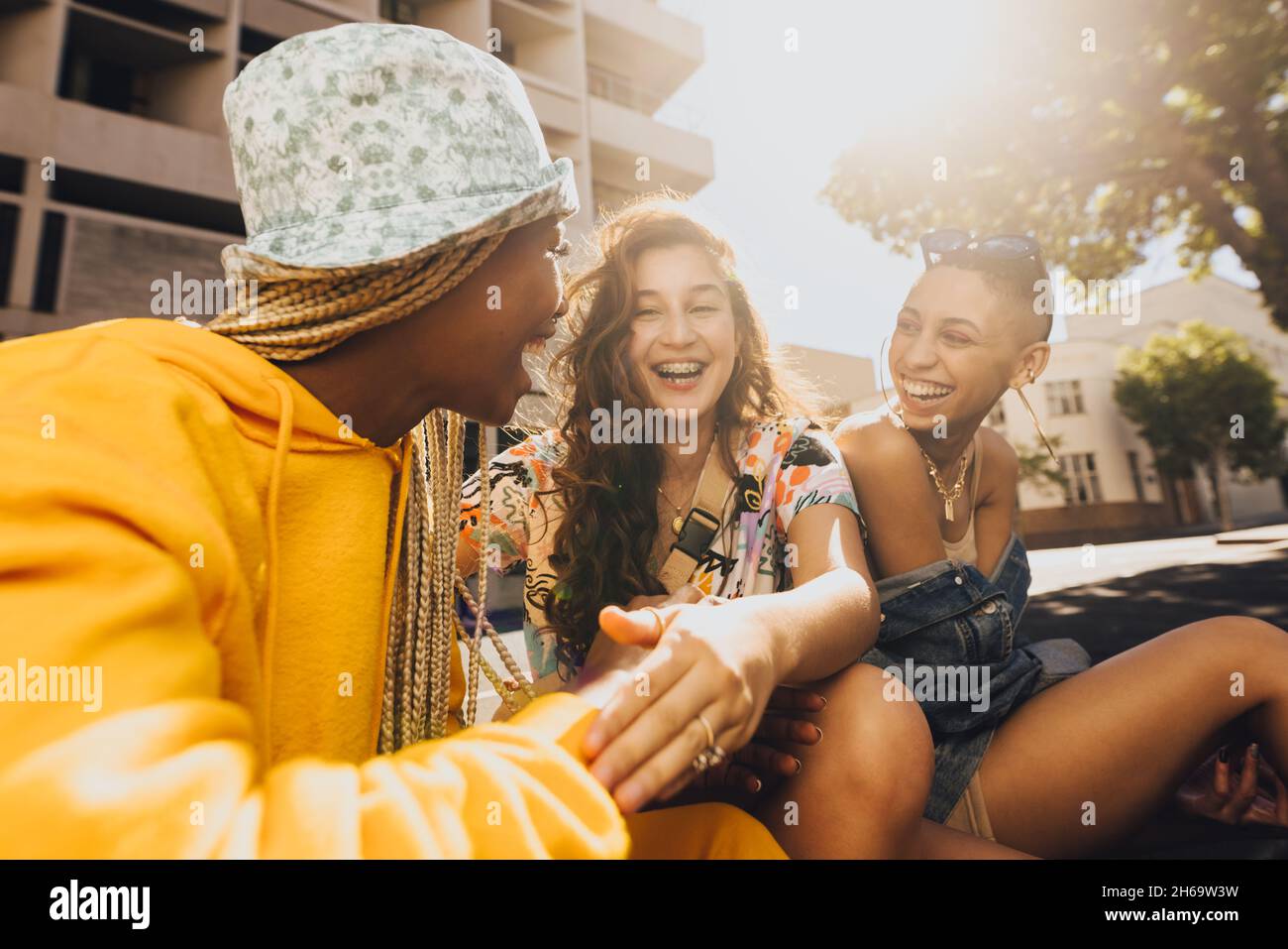 Sich mit Lachen verbinden. Eine Gruppe von Freunden der Generation z lacht fröhlich, während sie draußen in der Stadt zusammen hängen. Glückliche Freundinnen sitzen Stockfoto