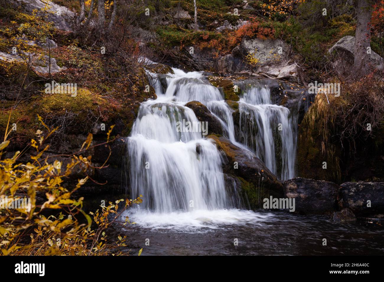 Der wunderschöne Kullaoja-Wasserfall fließt mitten in den Herbstfarben. Erschossen in der Nähe von Salla, Nordfinnland. Stockfoto