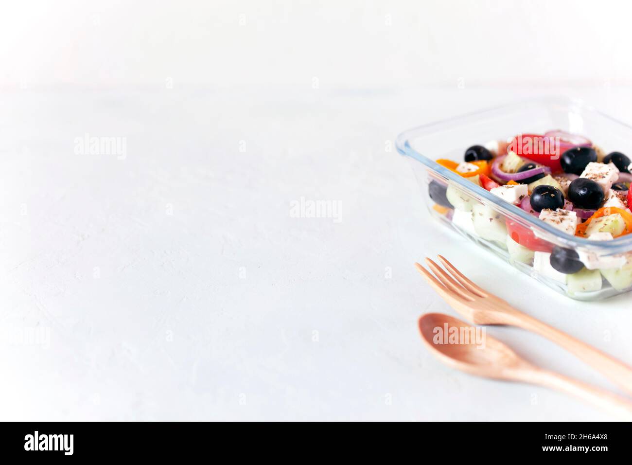 Lunchbox mit griechischem Salat, wiederverwendbarem Glasbehälter, Holzbesteck, auf weißem Hintergrund, Kopierraum Stockfoto