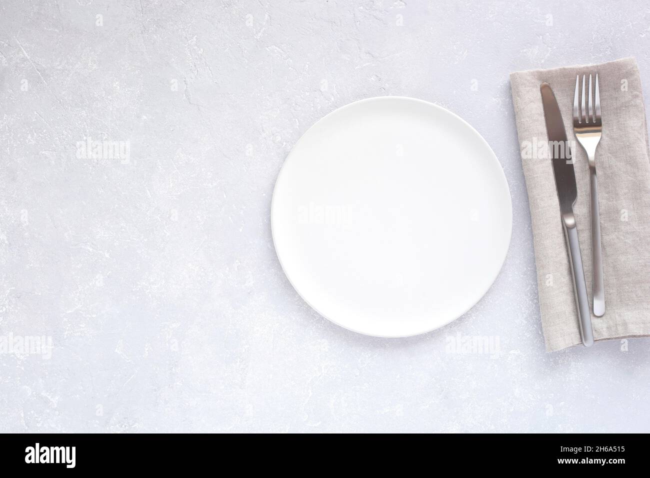 Leere, weiße runde Platte und silbernes Besteck auf hellgrauem Tischhintergrund, Draufsicht, Kopierraum Stockfoto