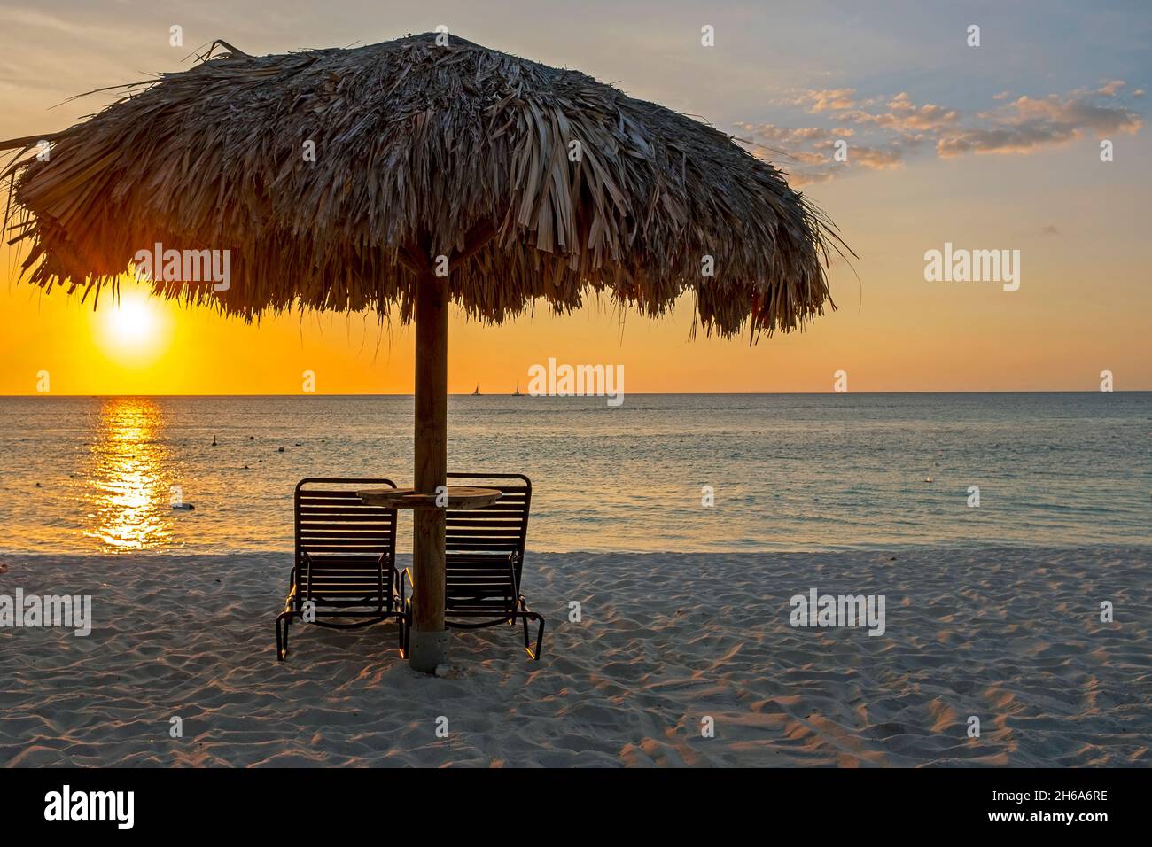 Strohschirm am Strand auf der Insel Aruba im Karibischen Meer bei Sonnenuntergang Stockfoto