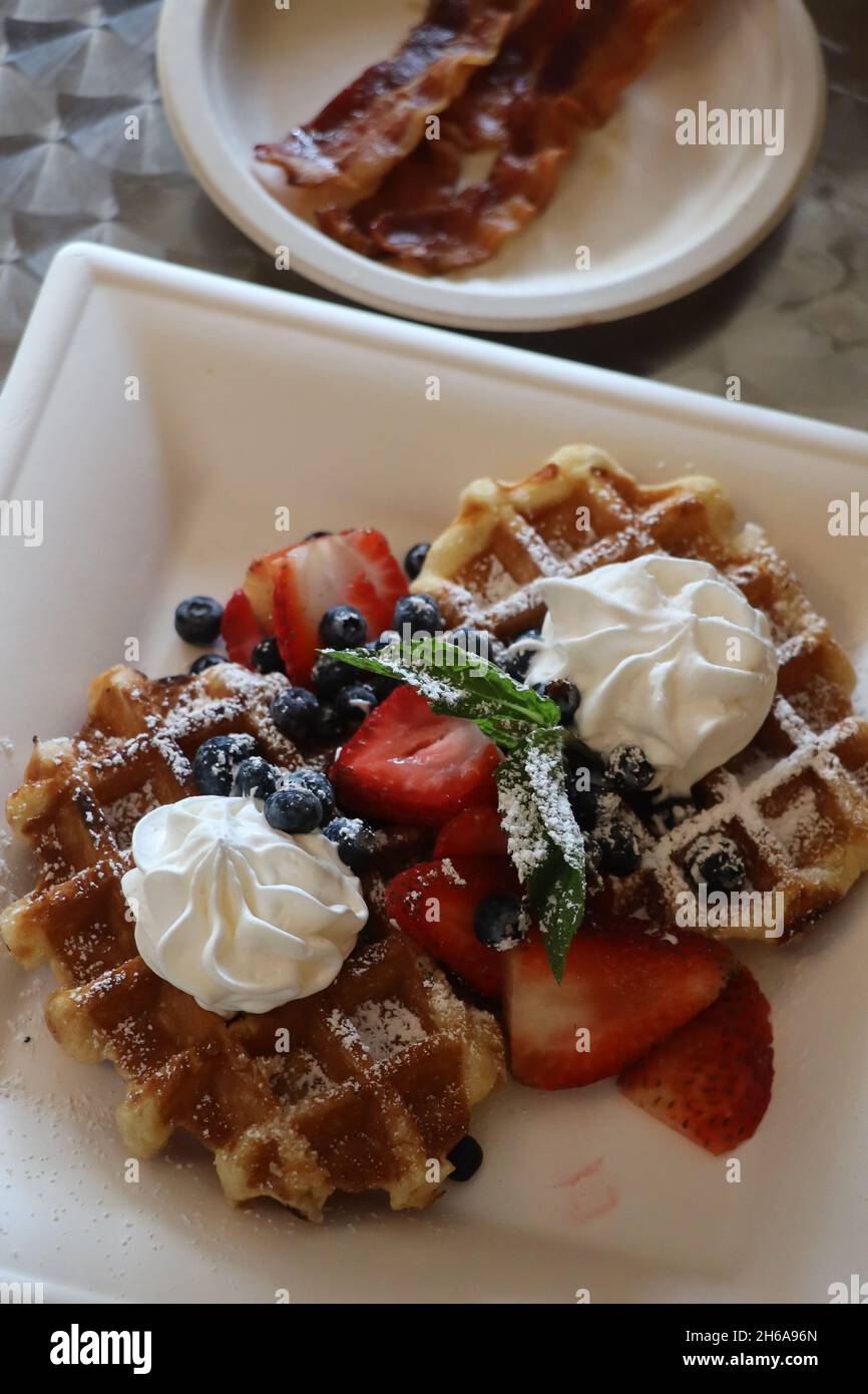 Leckere belgische Waffeln mit frischer Schlagsahne und Obst zusammen mit Speck auf der Seite Stockfoto